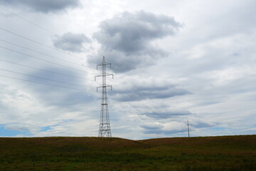 High tension electricity poles and cables over green grass field and gray cloudy sky in the countryside in Romania on summer day