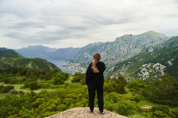 Fototapeta na wymiar Kotor, Montenegro - May 30, 2021: View of the back of a girl in a black tracksuit looking at Kotor and Koto-Bay bay