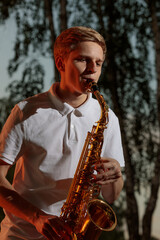 A young guy plays the saxophone in the evening at sunset