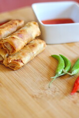 Fried chinese spring rolls placed on a kitchen chopping board and served with chilli sauce and fresh chili.