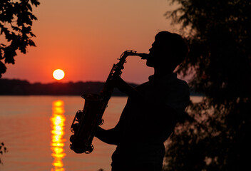 Silhouette of a young guy playing the saxophone in the evening at sunset
