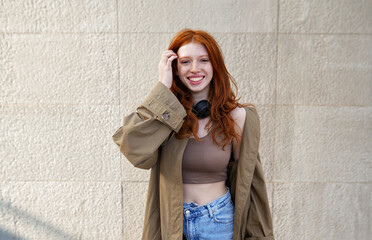 Happy teen stylish cool redhead fashion girl model standing on urban wall background looking at...