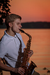 A young guy plays the saxophone in the evening at sunset