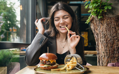 Attractive young woman eating french fries and a burger in a restaurant.
