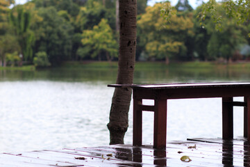 Long wooden benches and wooden decking that had been soaked in rain after the rain storm had passed leaving rain on the ground and on the benches making the area seem empty and uninhabited.