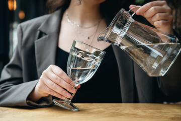 Close-up, a woman pours water into a glass in a cafe.