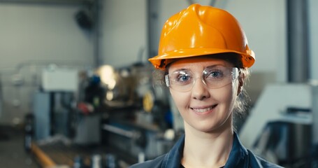 Portrait of a beautiful smiling female engineer in a protective vest and hard hat with goggles. Professional woman working in a modern manufacturing plant. CNC object