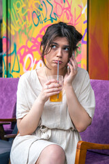 Funny young woman talking on the phone with a glass of lemonade.