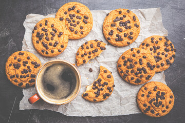 Homemade Chocolate chip cookies with coffee on paper over dark background, top view