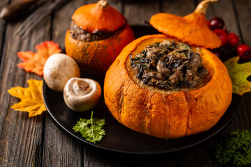 Tasty autumn stuffed pumpkin with fresh mushrooms, spinach and vegetables ready on rustic dark wooden table