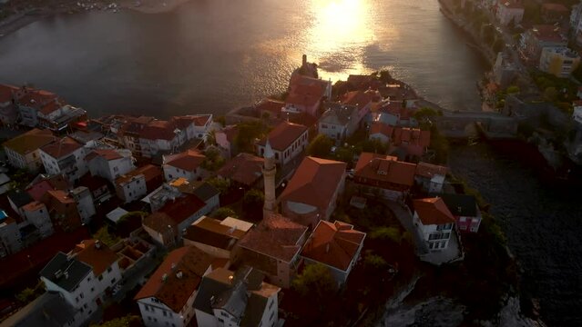 Flying over mosque and red rooftops of Amasra city, Turkey. Coastline of Black Sea province Bartin. Sun shine on sea surface in the harbor. 