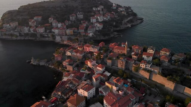Drone orbit around island near Amasra city, Bartin province, Turkey. Sun illuminating red rooftops and mosque at seaside