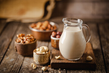 Vegan alternative non dairy milk from nuts in a jug with various nuts on wooden table