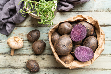 Close up of farm fresh purple potatoes in a paper bag on white wooden background, top view