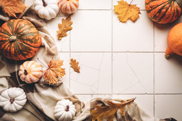 Cozy autumn flat lay with pumpkins, plaid and autumn leaves on tile background. Autumn home decor....