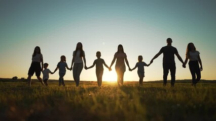 Happy family. Silhouette of large group of people at picnic in park. The family generation walks on the green grass. Parents and children play in nature. Family walking together across field at sunset