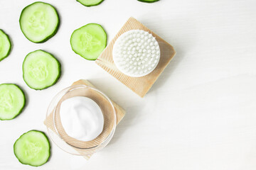 A sample of a moisturizing cosmetic product and a piece of green cucumber on a white wooden background with copy space. Body care, spa and beauty.