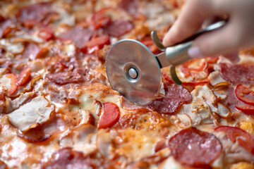Cutting delicious pizza with salami. Cutting pizza with a pizza cutter. Meat pizza cut into pieces