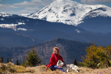 Naklejka premium Young beautiful girl resting with her Siberian husky dog together outdoor. Human and animal friendship concept. Snowy peak in the background