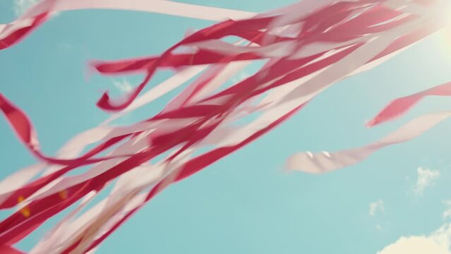 Red and white ribbons fluttering in the wind against blue sky in slow motion. Festive color ribbon design element. Traditional spring and summer fair decoration, suitable for street parties and