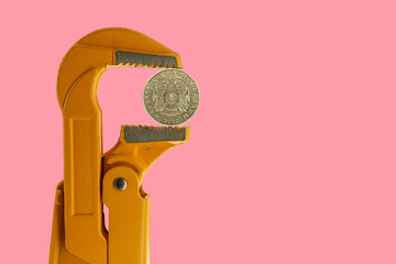 50 Kazakhstani tenge held in an orange plumber wrench on a pink background. Emblem of Kazakhstan