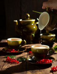 Pouring milk into the cup of vintage green set on the wooden table