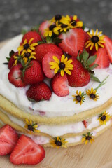 tiered layered cake with yellow wildflowers and strawberries with white frosting icing on wood board summer cake rustic minimalist - naked cake