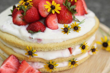 tiered layered cake with yellow wildflowers and strawberries with white frosting icing on wood board summer cake rustic minimalist - naked cake