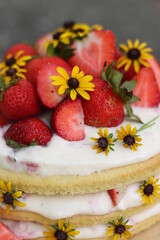 tiered layered cake with yellow wildflowers and strawberries with white frosting icing on wood board summer cake rustic minimalist - naked cake