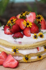 tiered layered cake with yellow wildflowers and strawberries with white frosting icing on wood board summer cake rustic minimalist - naked cake