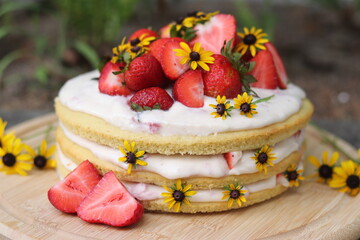 tiered layered cake with yellow wildflowers and strawberries with white frosting icing on wood...