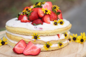 tiered layered cake with yellow wildflowers and strawberries with white frosting icing on wood board summer cake rustic minimalist - naked cake