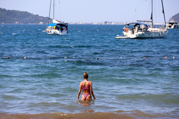 Girl in bikini going to swim in sea water, vacation on summer beach of Mediterranean coast. View to...