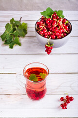 Red currant compote in a glass and a berry in a bowl on the table. Homemade summer drinks. Vertical view