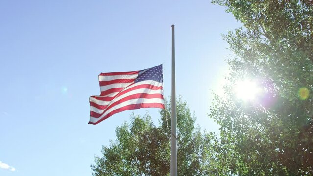 American flag dramatically waves at half mast with bright hopeful sun flaring
