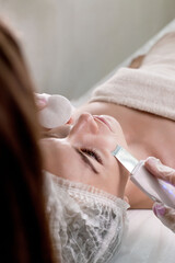 Cosmetologist, beautician making facial treatment with ultrasonic spatula to young woman,face skin scrubber treatment with ultrasonic spatula,facial cleansing procedure in beauty salon