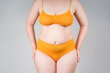 Fat woman in orange underwear on gray background, overweight female body - obrazy, fototapety, plakaty