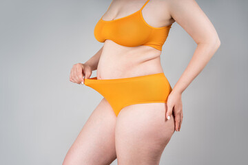 Fat woman in orange underwear on gray background, overweight female body
