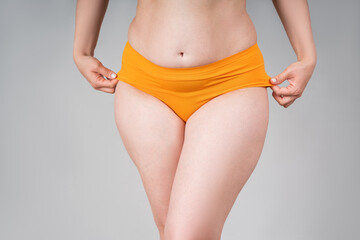 Fat woman in orange panties on a gray background, thick female thighs - obrazy, fototapety, plakaty
