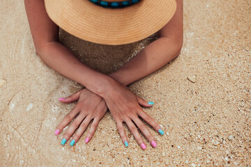 Beautiful female hands with pink and blue manicure nails on sea sand background
