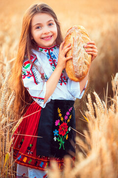 Beautiful girl woman in traditional Bulgarian folklore dress holding homemade bread in wheat field
