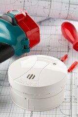 Smoke detector or fire alarm sensor on white architectural plans background with drill and...