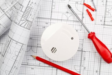 Smoke detector or fire alarm sensor with rolls of architectural drawing background with tools and...