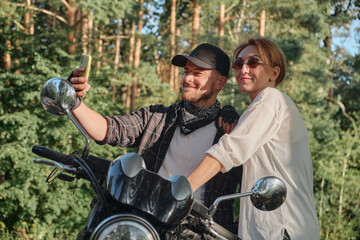 Fototapeta na wymiar Middle age couple riding a motorcycle having fun and taking a selfie on a mobile phone camera