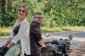Naklejka premium Middle age couple talking and having fun, sitting on a motorcycle, traveling together on a forest road
