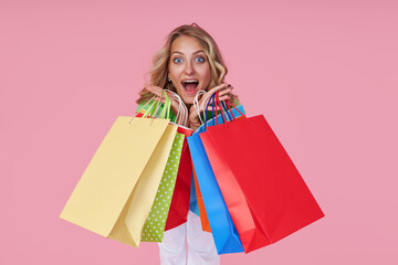 Portrait of an excited joyful young woman with colorful shopping bags on a pink background. Surprised Girl with wide open mouth