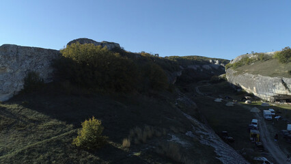 Rock above gorge. Shot. Top view of landscape of stone ridge hills, blue sky and green gorge. Sunny day in mountain gorge