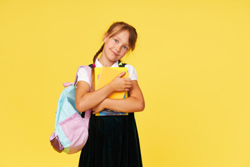 Portrait of a schoolgirl with textbooks and a backpack on a yellow background. Back to school