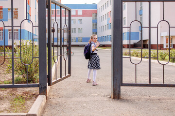 Back to school. Girl in school uniform go to school with backpack behind their backs. Kid waving her hand saying bye. Beginning of lessons. First day of autumn. Elementary school student. 