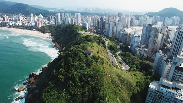 Ilha do Tombo com pessoas circulando pela praia e muitas ondas com vegeta&ccedil;&atilde;o ao redor. 